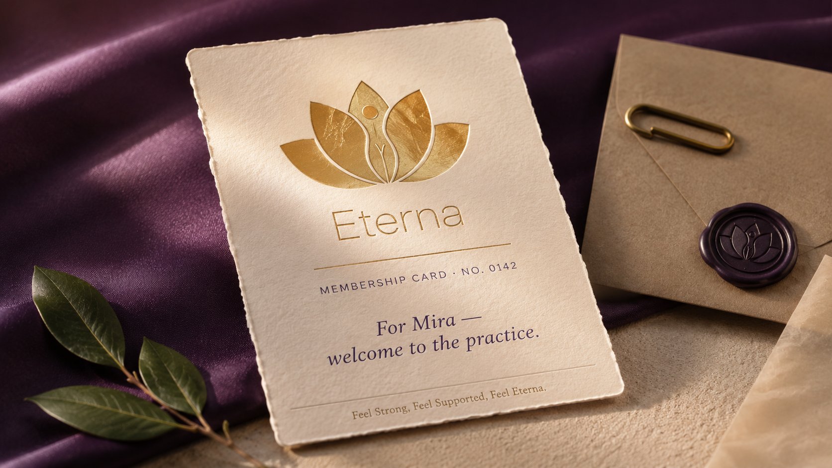 ETERNA membership welcome card macro hero, cream deckled-edge cotton card with the lotus+figure mark and Eterna wordmark in antique-brass hot-foil emboss, Membership Card · No. 0142 in small caps, For Mira welcome to the practice in elegant serif italic, Feel Strong Feel Supported Feel Eterna tagline, dusty-plum silk under-surface, kraft envelope with deep-purple wax seal of the lotus mark, bay laurel leaf